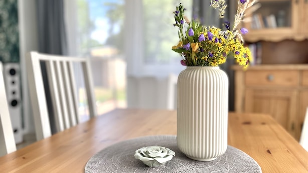 Una mesa de comedor con un jarrón blanco con flores, un mantel individual y una servilleta blanca.