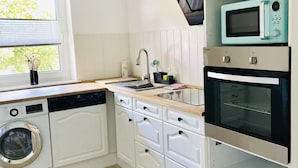 Cocina compacta con muebles blancos, lavadora, microondas y horno.