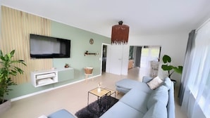 Una sala de estar moderna con un sofá grande azul claro, un televisor de pantalla plana montado en la pared y una lámpara colgante.