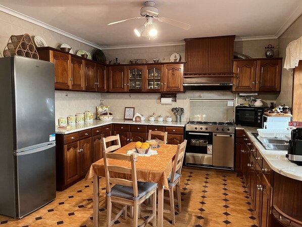 A kitchen with wooden cabinets, a stainless steel refrigerator, a dining table with chairs, and a tiled floor.