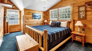 Acogedora habitación estilo cabaña con cama, banco de madera, ventilador de techo y ventana con vistas al exterior.