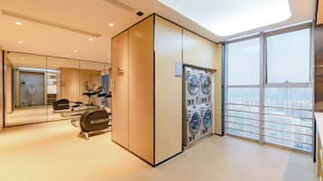 A modern hotel room with a large window, a built-in washer and dryer, and a mirror reflecting the room.