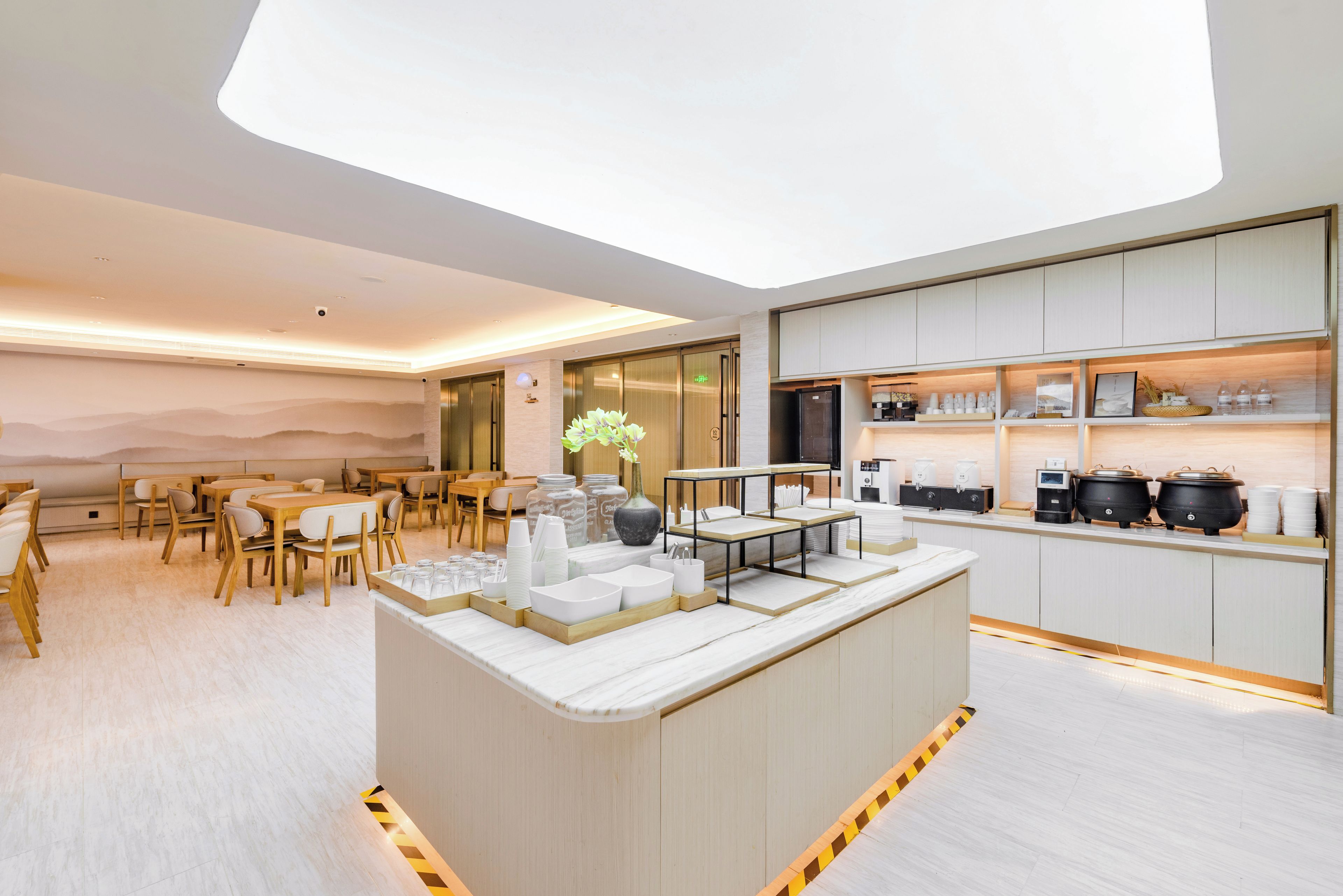 A modern hotel lobby with a central bar area, seating arrangements, and a kitchen counter with various items.