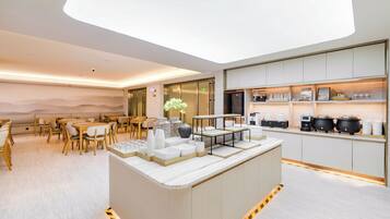 A modern hotel lobby with a central bar area, seating arrangements, and a kitchen counter with various items.