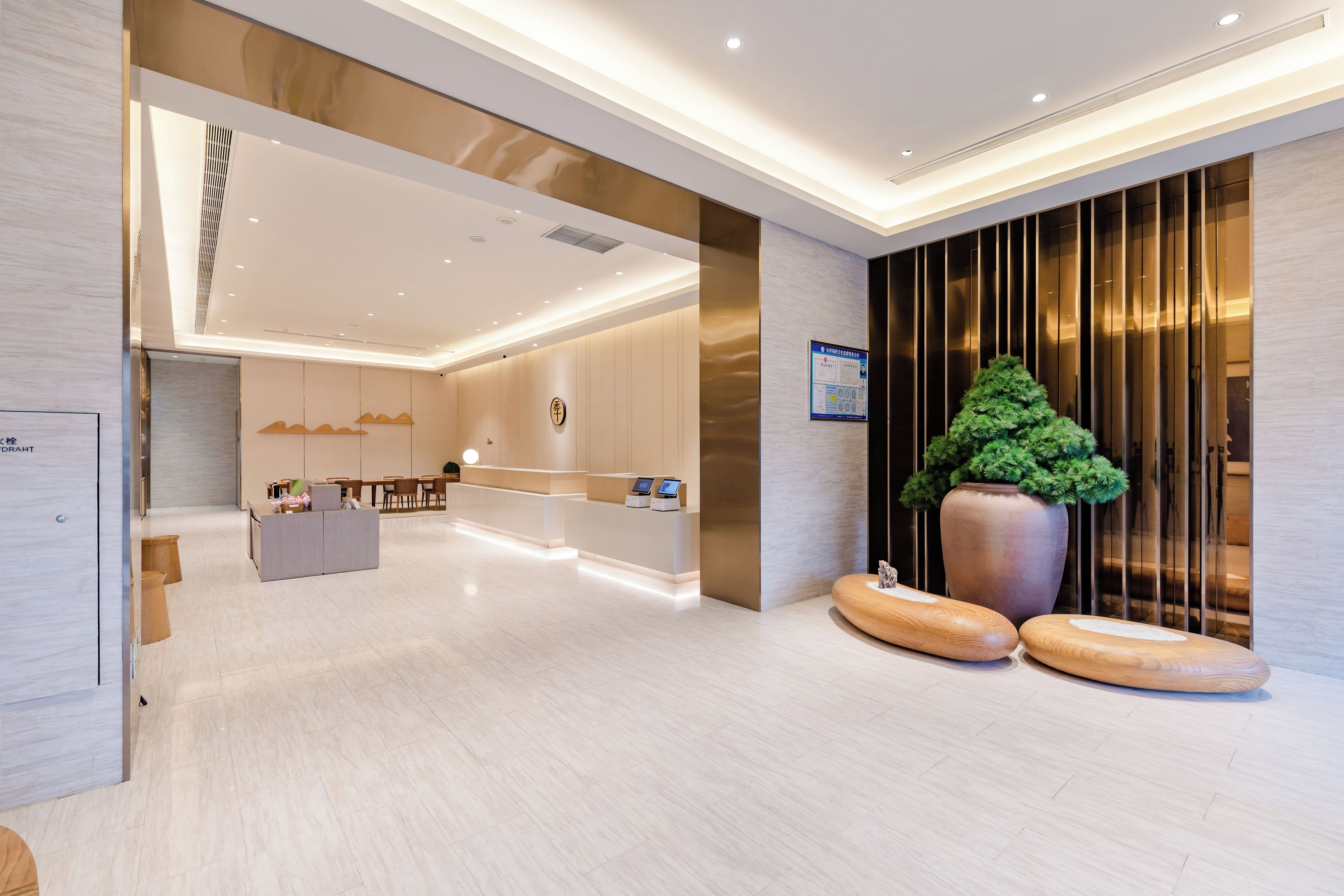 A modern hotel lobby with a reception desk, seating area, and a large potted plant.