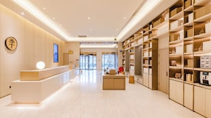 Un hall d’hôtel moderne avec un comptoir d’accueil, un écran numérique et une grande bibliothèque.