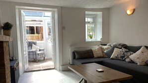 A living room with a sofa, a coffee table, and a fireplace. There is a door leading to an outdoor area with a chair and a plant.