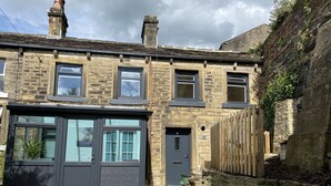 A traditional stone house with a dark front door, multiple windows, and a small front garden.
