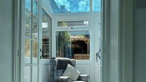 A room with a view of the sky through a large window, a plaid armchair, and a wooden door.