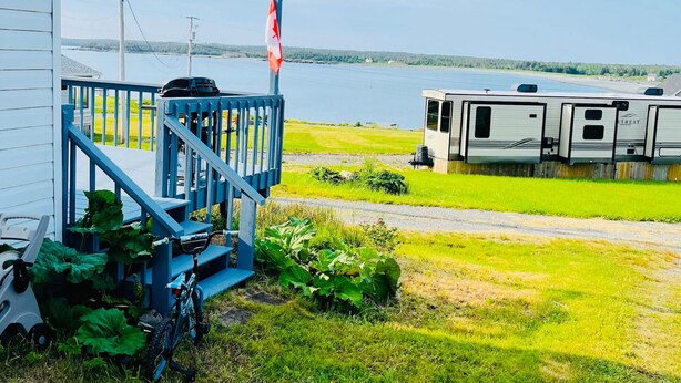 Un bâtiment blanc avec un escalier bleu et un drapeau canadien. Devant, il y a une pelouse où l’on peut voir un vélo et une remorque.