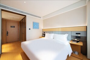 A modern hotel room with a large bed, bedside tables, a nightstand, a headboard, and a door leading to another room. - Ji Hotel (Shenyang)