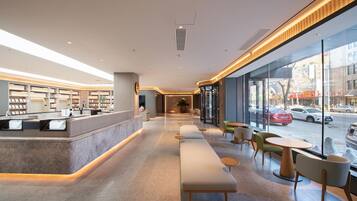 A modern hotel lobby with a reception desk, seating area, and large windows offering a view of the street.