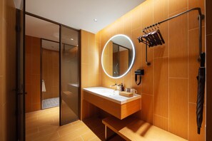 A modern bathroom with a glass shower door, a round mirror with a light, a wooden vanity, and a towel rack. - Ji Hotel (Shenyang)