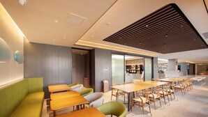 A modern dining area with wooden tables and green and white chairs, a kitchen in the background, and a ceiling with a wooden slat design. - Ji Hotel (Shenyang)