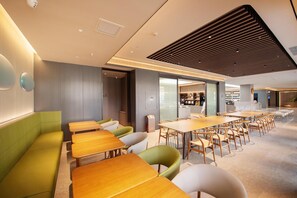 A modern dining area with wooden tables and green and white chairs, a kitchen in the background, and a ceiling with a wooden slat design. - Ji Hotel (Shenyang)