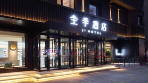 Entrada de hotel com design moderno, destacando fachada de vidro e letreiros iluminados.