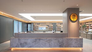 A modern reception desk with a marble base, a wooden panel wall, and a large circular sign with Chinese characters. - Ji Hotel (Shenyang)