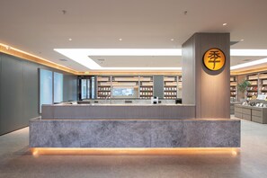 A modern reception desk with a marble base, a wooden panel wall, and a large circular sign with Chinese characters. - Ji Hotel (Shenyang)