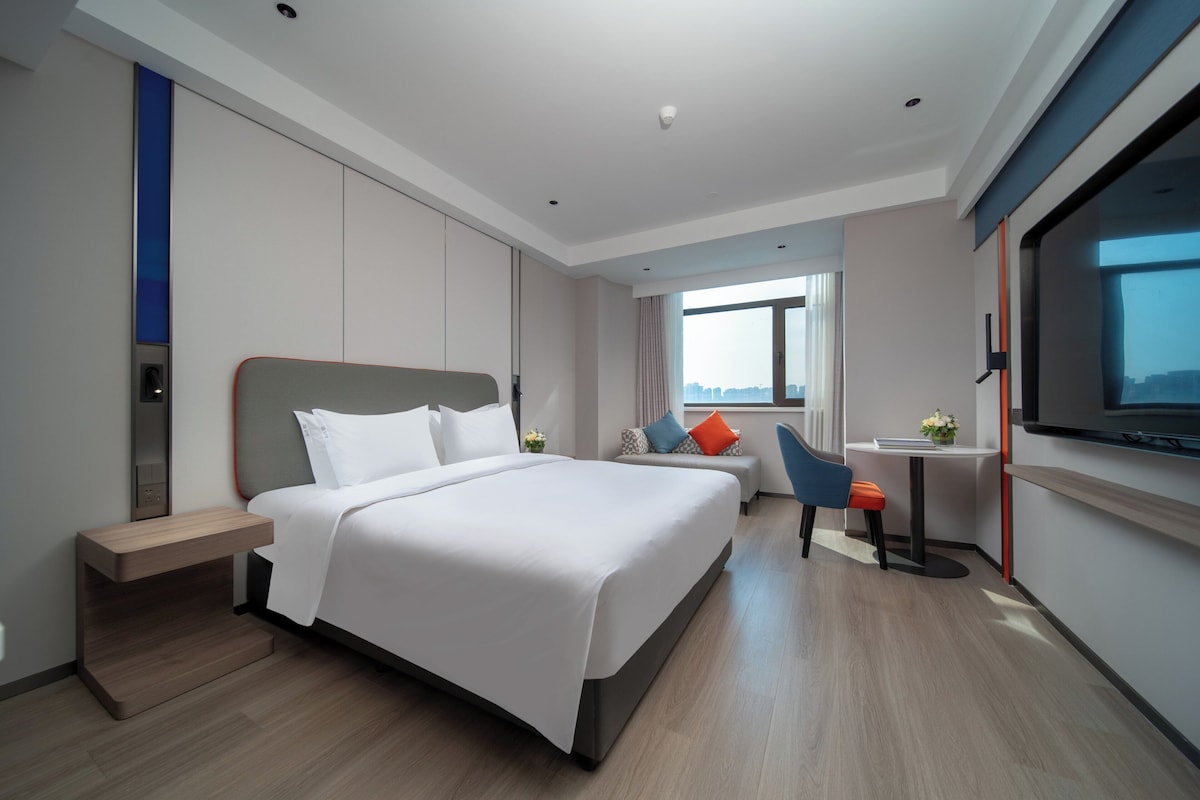 A modern hotel room with a large bed, a desk, and a TV.