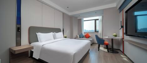 A modern hotel room with a large bed, a desk, and a TV.