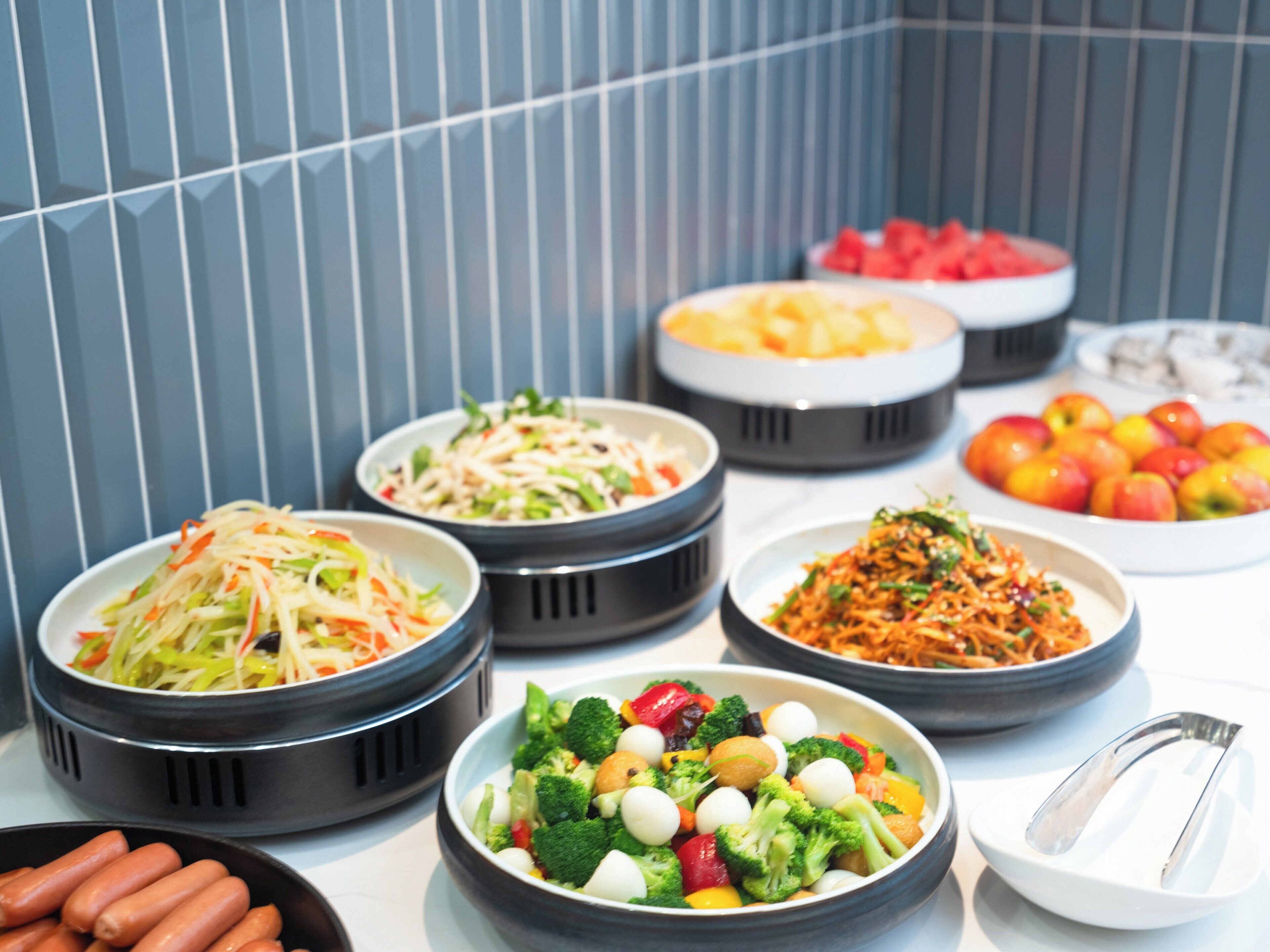 Un bufé con diversos platos, incluyendo ensaladas, frutas y verduras.