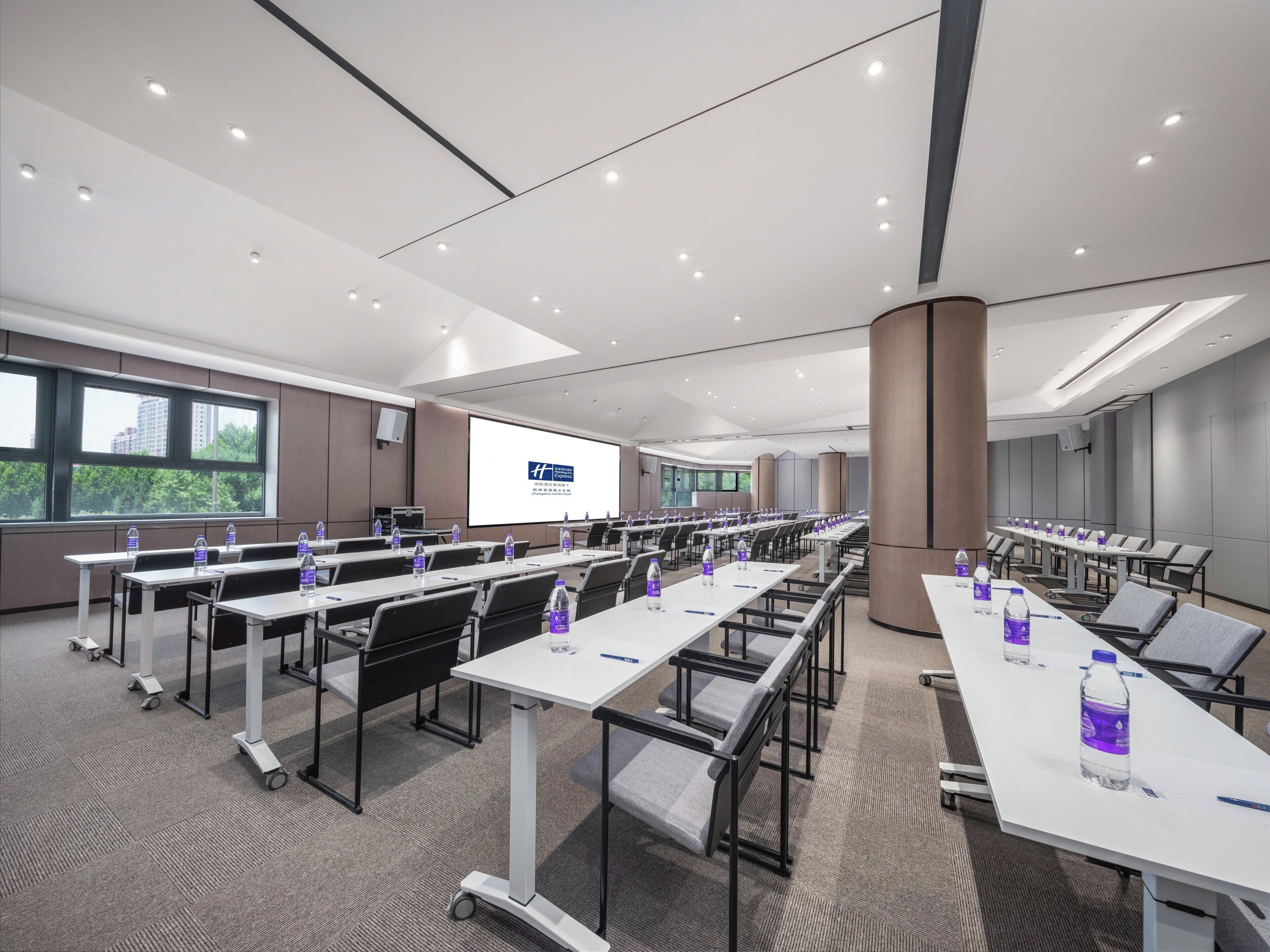Une salle de conférence équipée de plusieurs tables, de chaises et d’un grand écran pour les présentations.