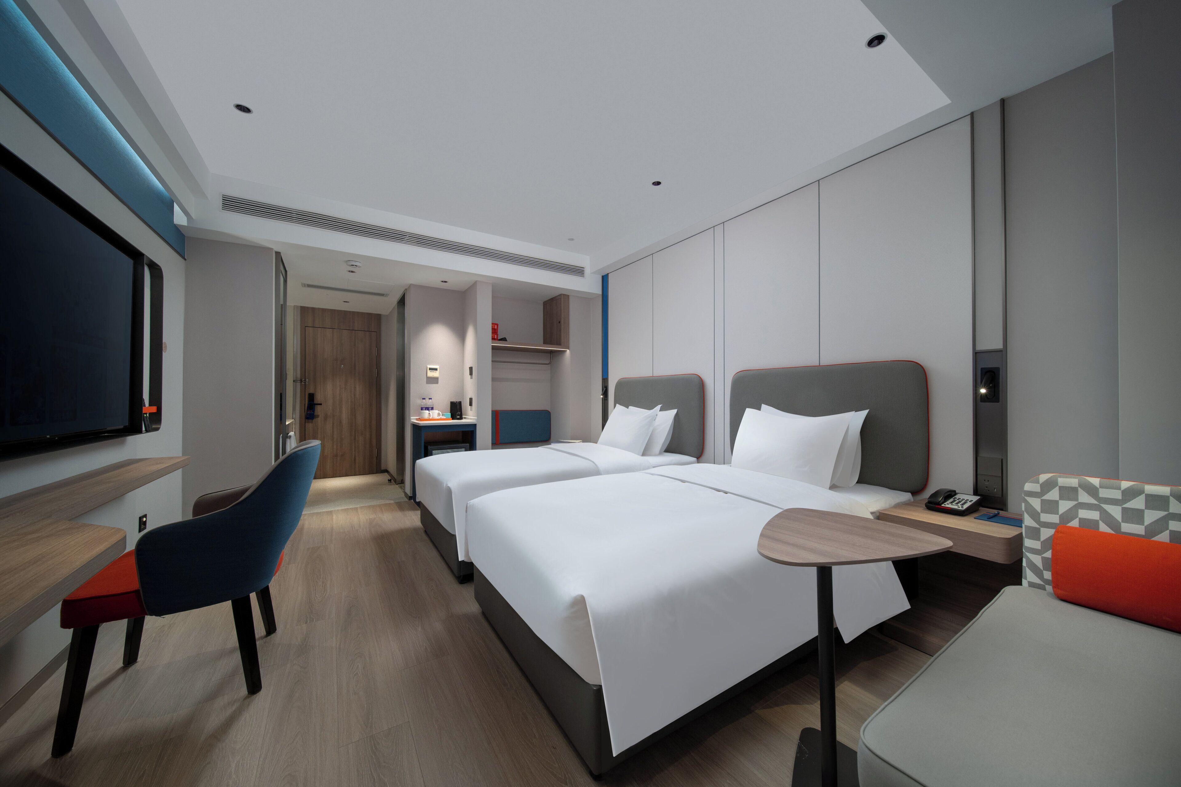 A modern hotel room with two beds, a desk, a chair, and a TV.