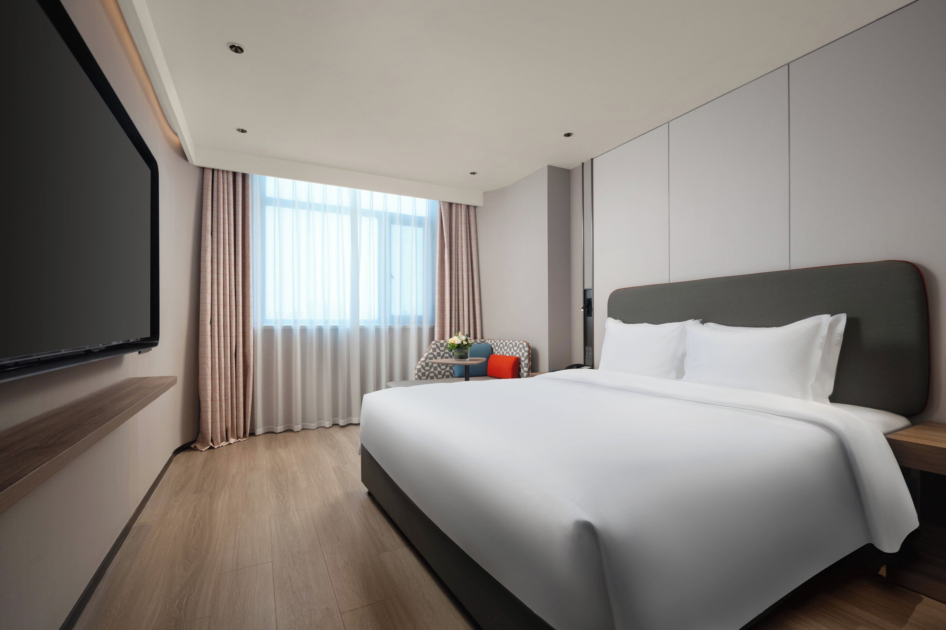 Een moderne hotelkamer met een groot bed, een flatscreen televisie aan de muur en een raam met gordijnen.