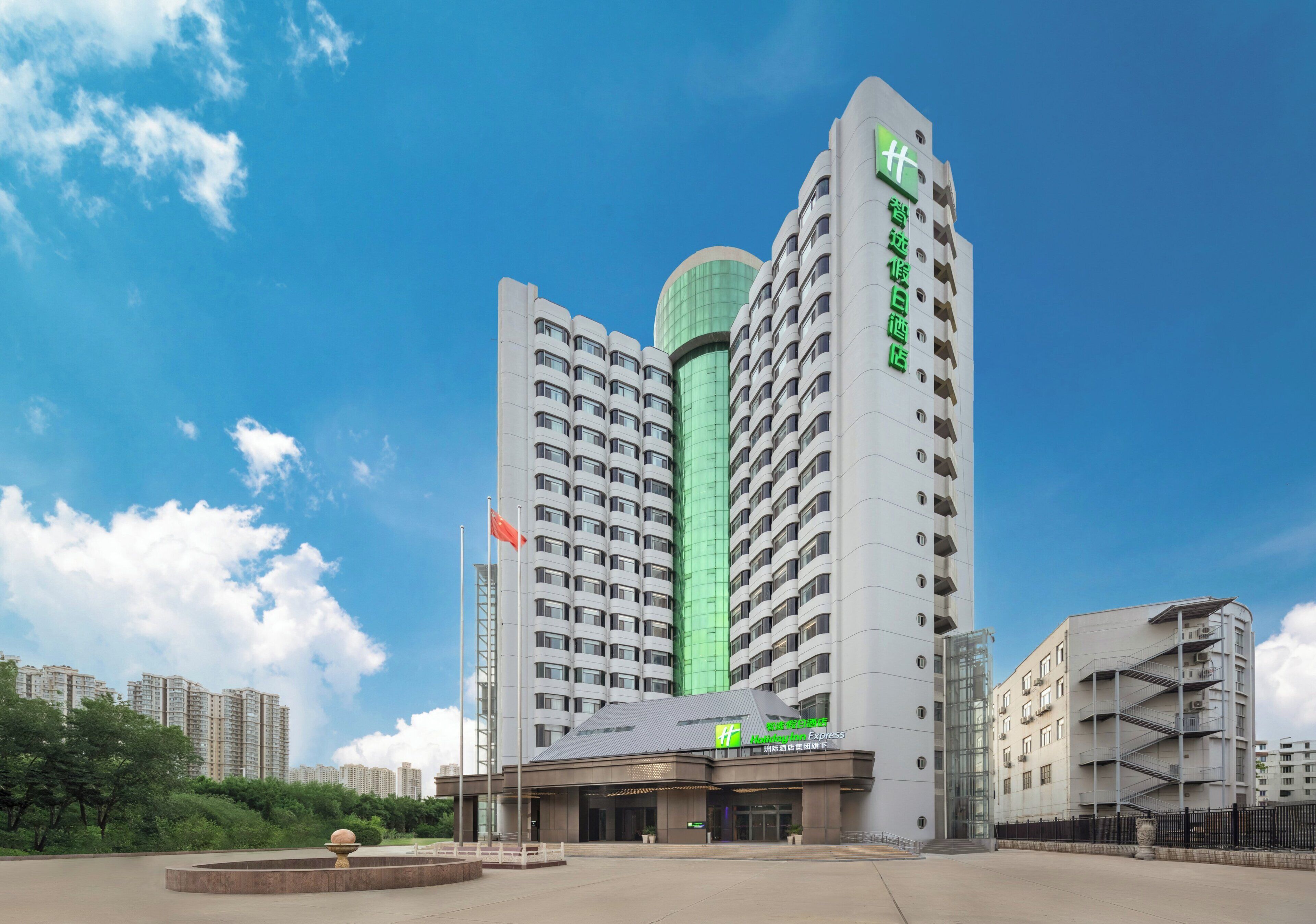 A modern hotel with a prominent green and white facade, multiple floors, and a clear sky.