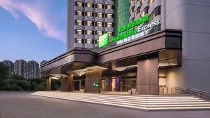 Un hotel Holiday Inn Express con una facciata moderna, un ingresso illuminato e una vista chiara dei grattacieli circostanti.