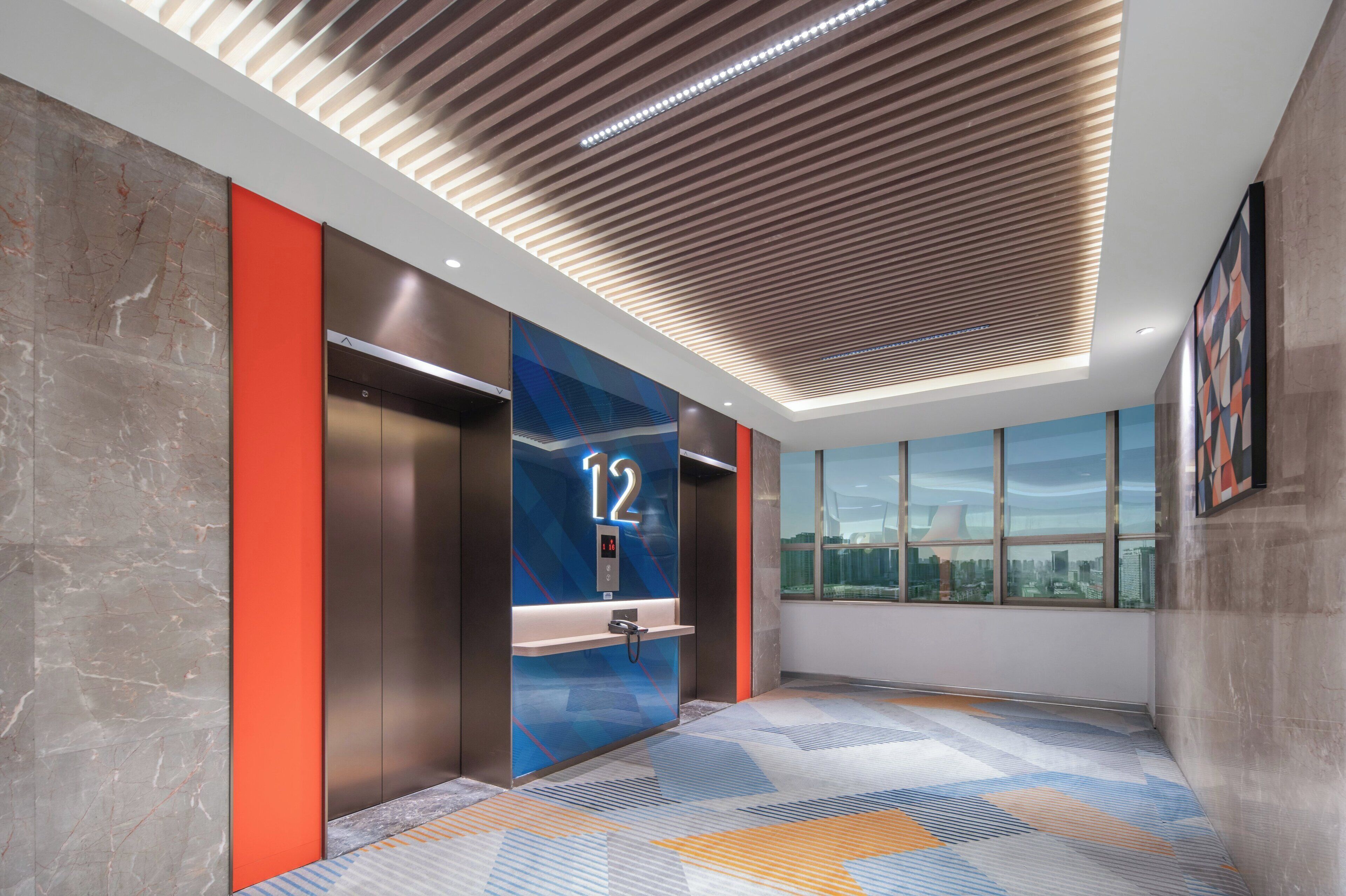 A modern elevator with a digital display showing the number 12, a patterned floor, and a city view through large windows.