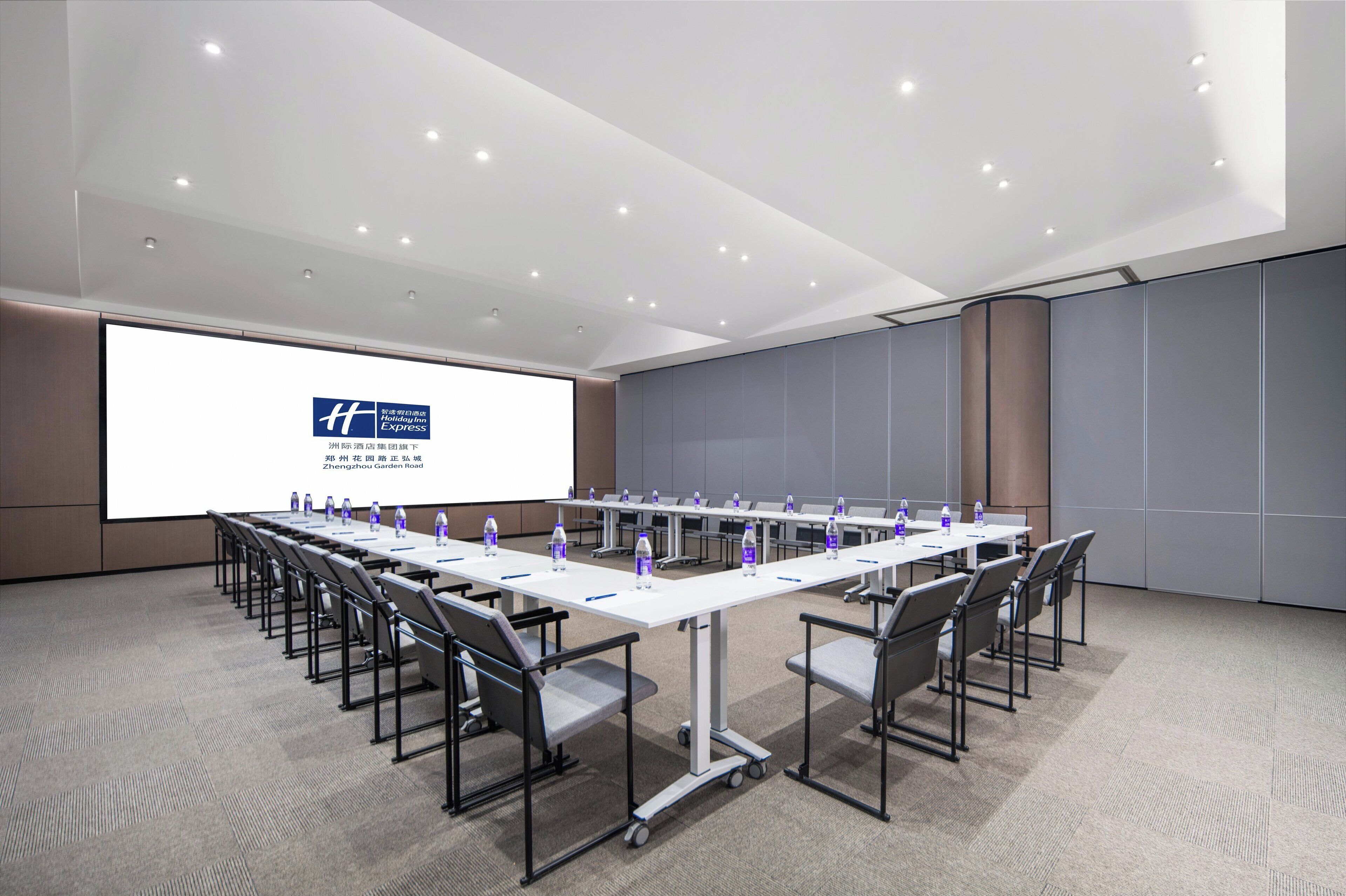 A conference room with a long table, chairs, and a projector screen displaying a logo.