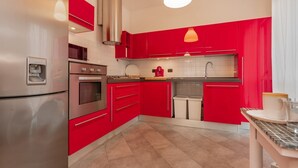 A modern kitchen with red cabinets, stainless steel appliances, and a tiled backsplash.