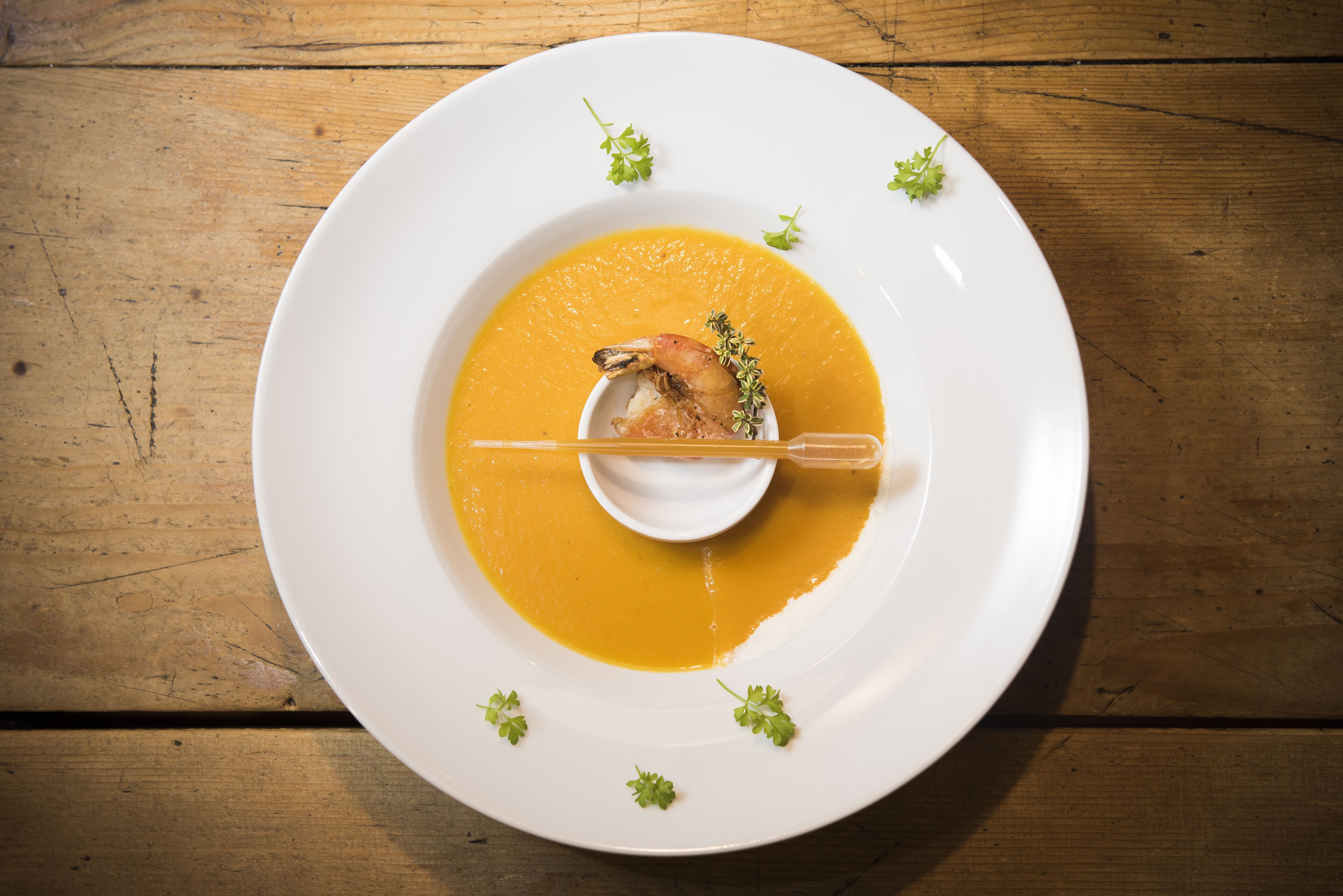Un plato blanco con una crema anaranjada, adornado con perejil, sobre una mesa de madera.