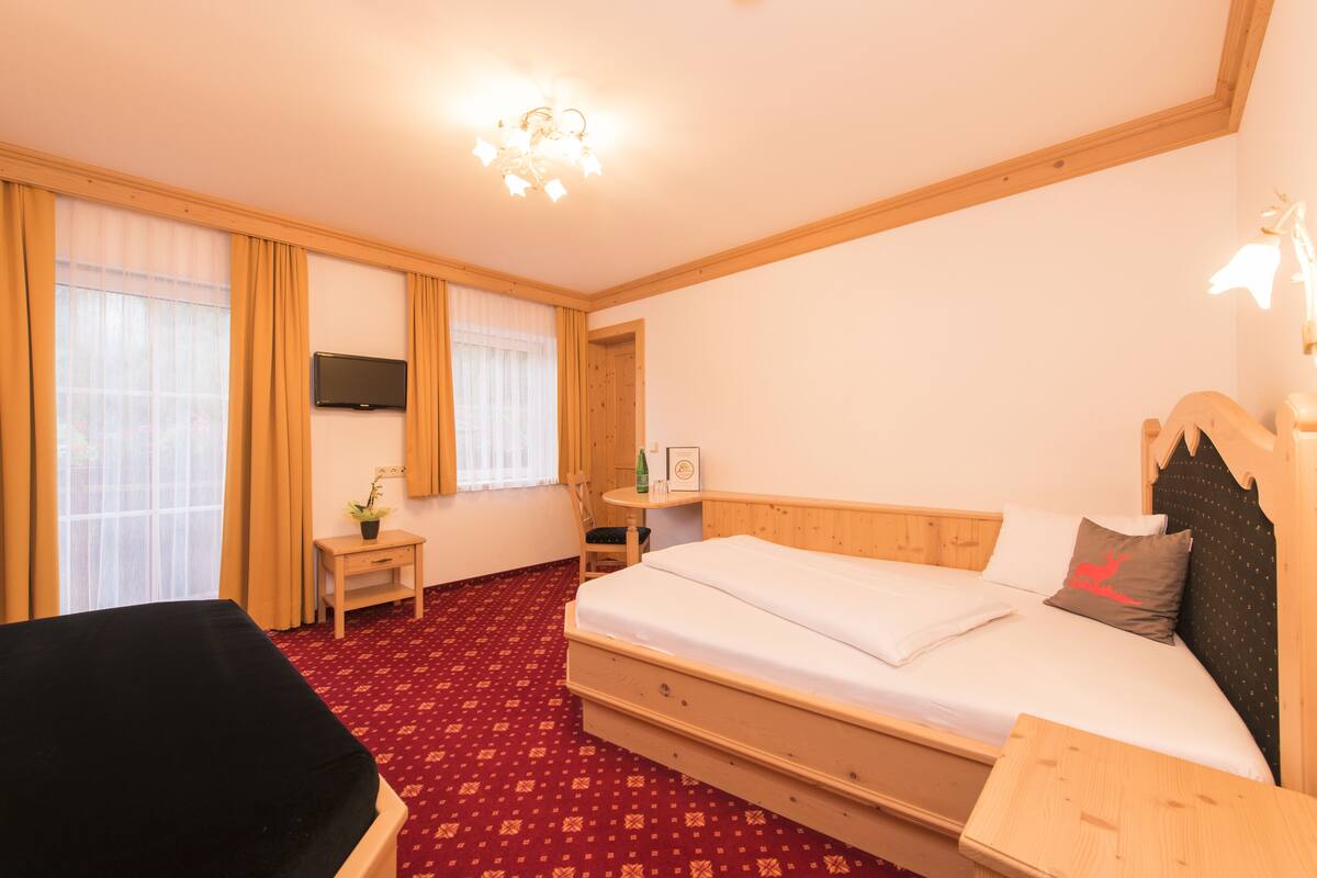 Una habitación de hotel con cama, escritorio, silla, televisor y piso cubierto de alfombra roja.