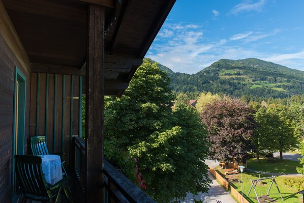 Un balcón de madera con una mesa y sillas, con vistas a un paisaje verde exuberante con árboles y una montaña al fondo.
