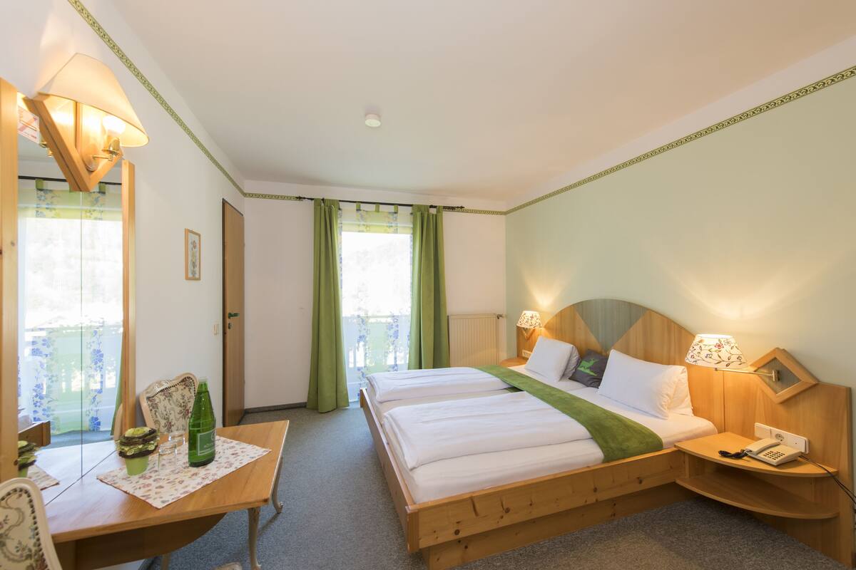 Habitación de hotel con dos camas, un escritorio de madera, una silla, una mesa con mantel individual, un teléfono y una lámpara.