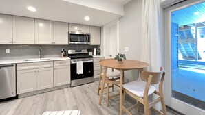Eine moderne Küche mit weißen Schränken, einer Edelstahl-Mikrowelle und einem schwarzen Backofen. Ein Holztisch mit zwei Stühlen steht daneben.
