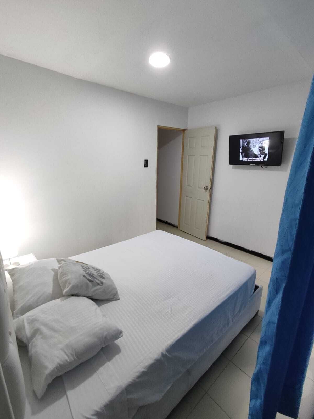 Ein Schlafzimmer mit einem Bett, Kissen, einem Fernseher an der Wand und einer Tür im Hintergrund.