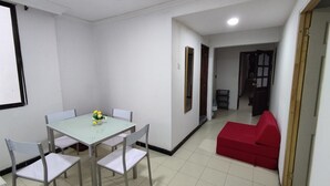 Uma sala de jantar com mesa e cadeiras, um sofá vermelho e um corredor que dá para uma cozinha.