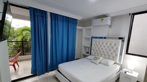 Quarto de hotel com cama, mesa de cabeceira, ar condicionado fixado na parede e varanda com cortinas azuis.