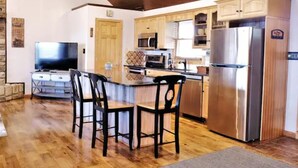A modern kitchen with wooden cabinets, a stainless steel refrigerator, a microwave, and a dining area with four chairs. - Tranquil Cabin on Barren River Lake (Glasgow)