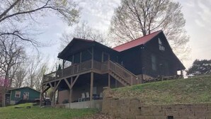 A two-story building with a balcony and a red roof, surrounded by trees and a grassy area. - Tranquil Cabin on Barren River Lake (Glasgow)