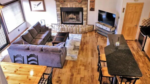 A cozy living room with a stone fireplace, a sofa, a TV, and a dining area with a table and chairs. - Tranquil Cabin on Barren River Lake (Glasgow)