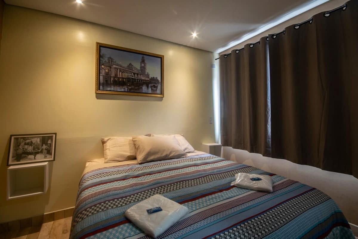 Una habitación de hotel con una cama, un cuadro en la pared y una ventana con cortinas.