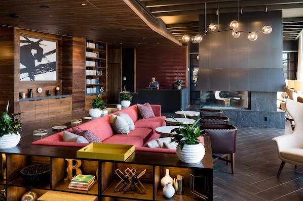 A modern lounge area with a red sofa, bookshelves, a fireplace, and a bar area. - Cambria Hotel Boston Somerville (Somerville)