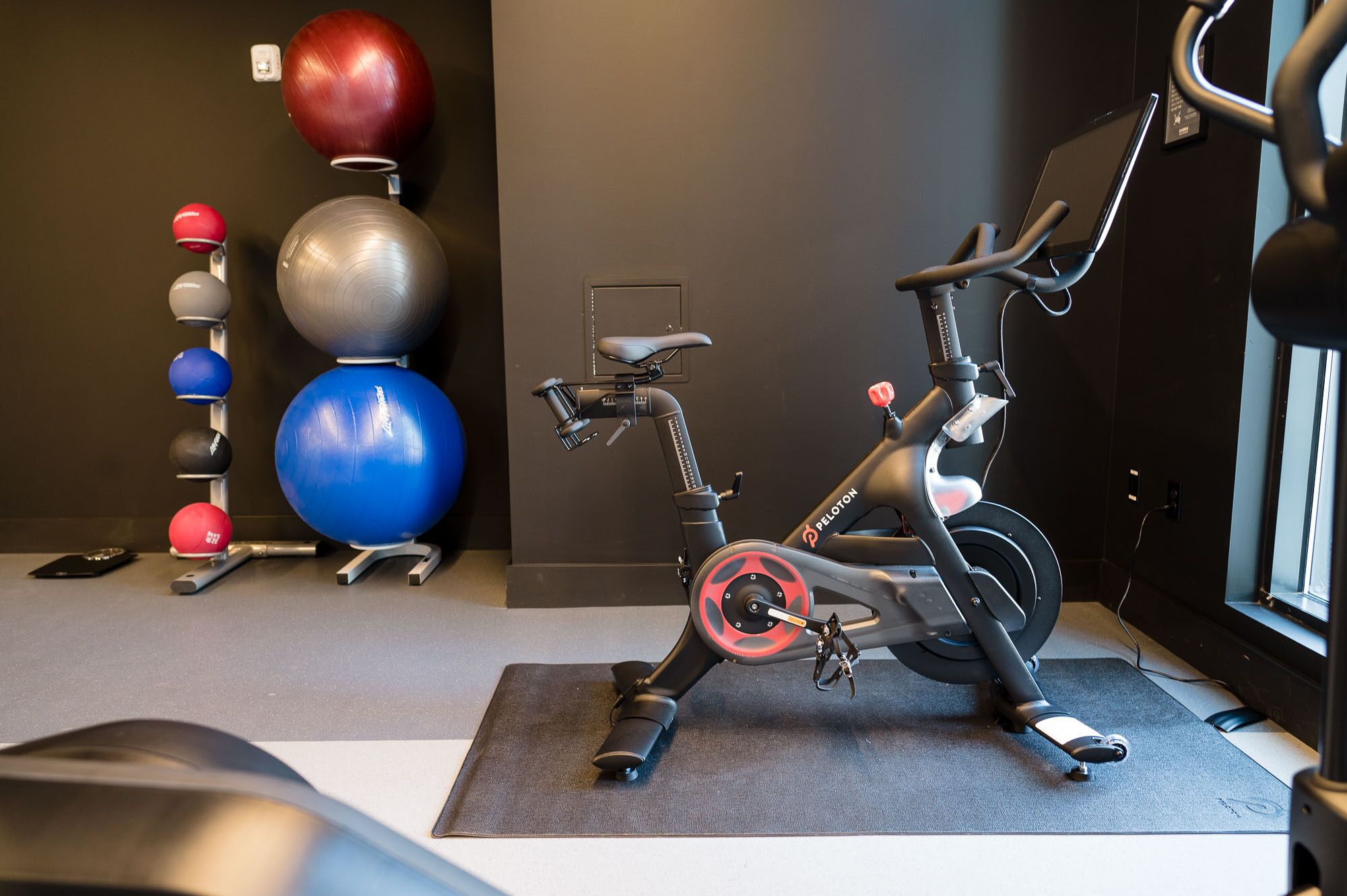 En motionscykel, träningsbollar och en väggmonterad lampa i ett gym.