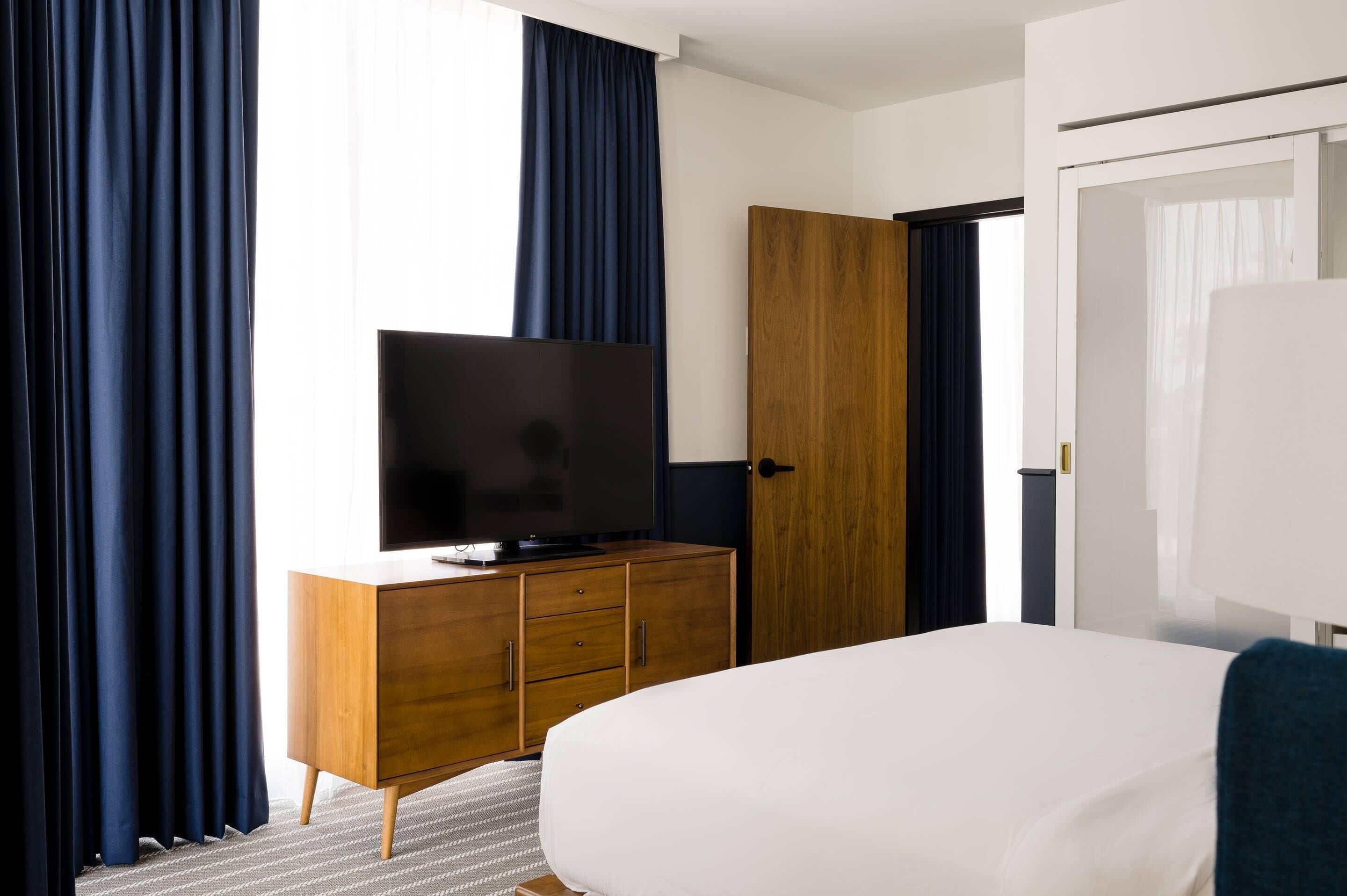 A hotel room with a bed, a television on a wooden dresser, a wardrobe, and a door.