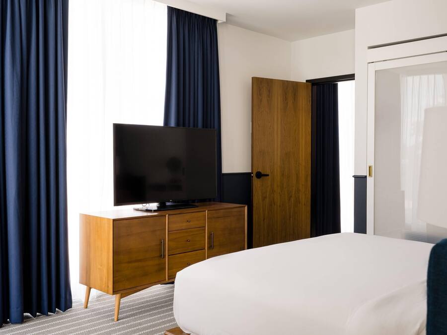 Ein Hotelzimmer mit einem Bett, einem Fernseher auf einer Holzkommode, einem Kleiderschrank und einer Tür.