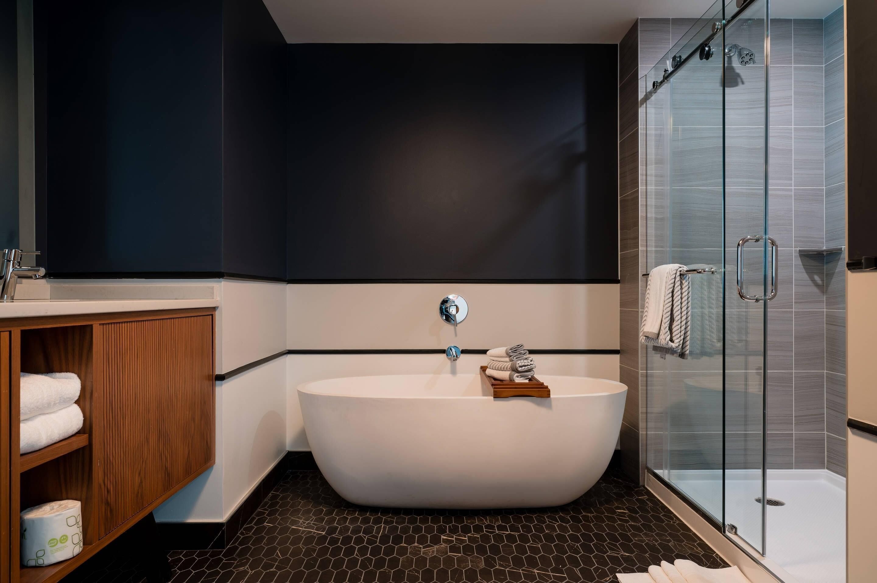 A modern bathroom with a freestanding bathtub, a glass shower enclosure, and a wooden vanity with towels.